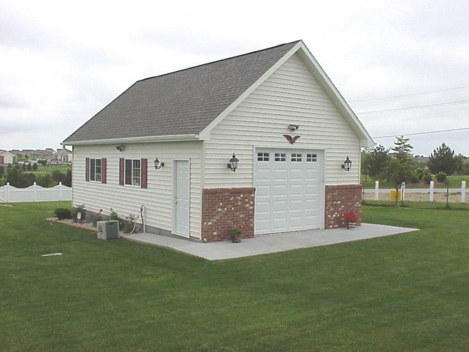 Two-car garage with white siding, brick accents, and a gray roof on a green lawn.