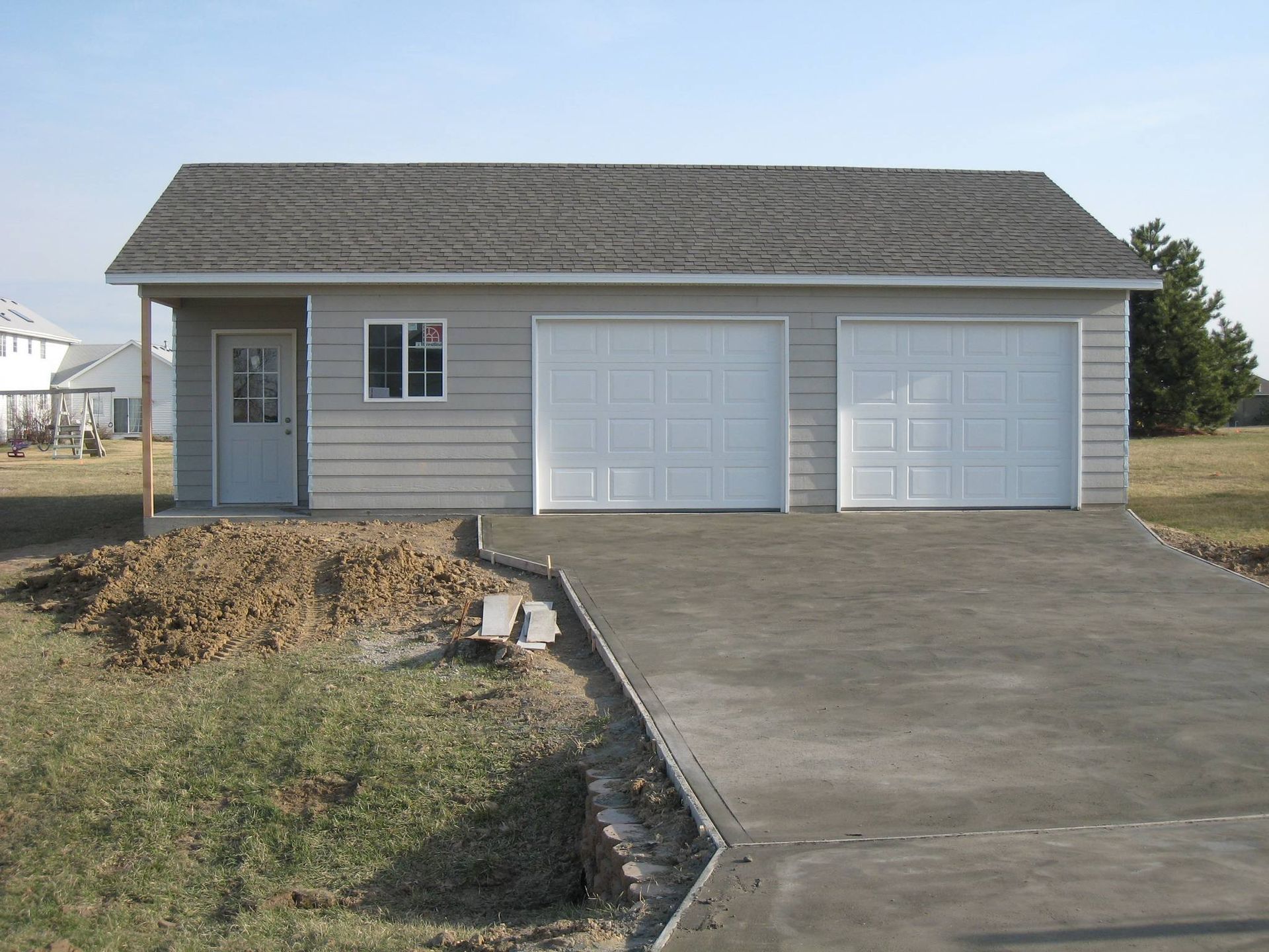 Two-car garage with gray siding and roof, white doors, and a concrete driveway.