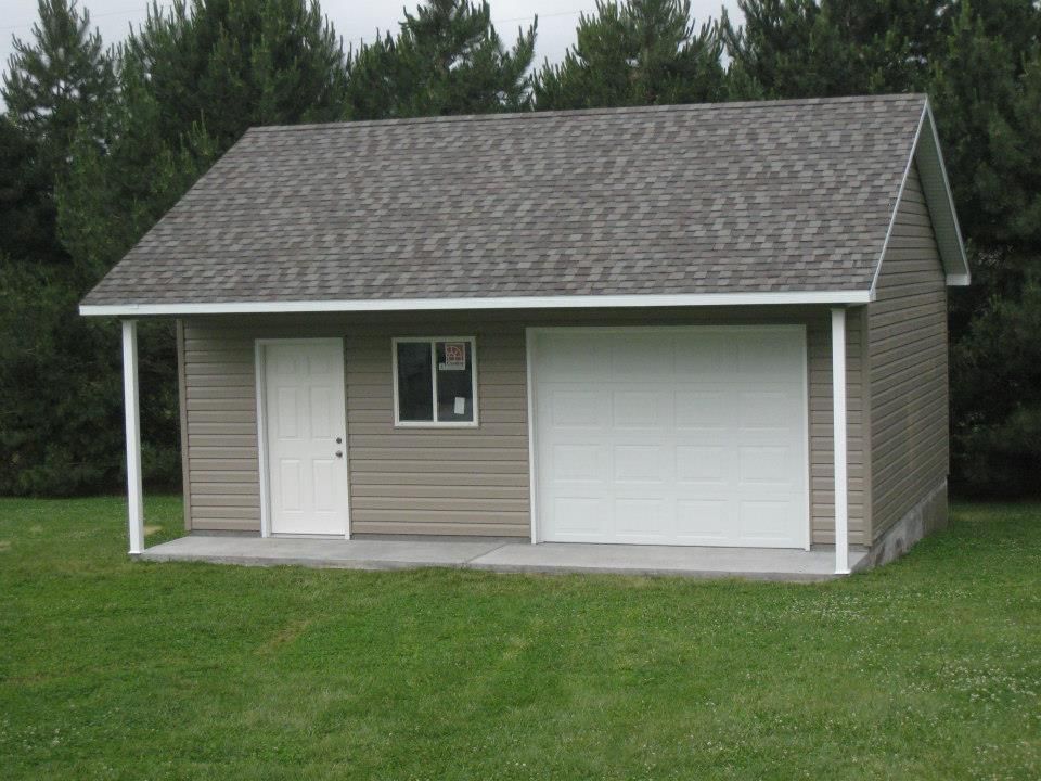 Tan-sided detached garage with white door and garage door. Gray roof, small window. Green lawn.