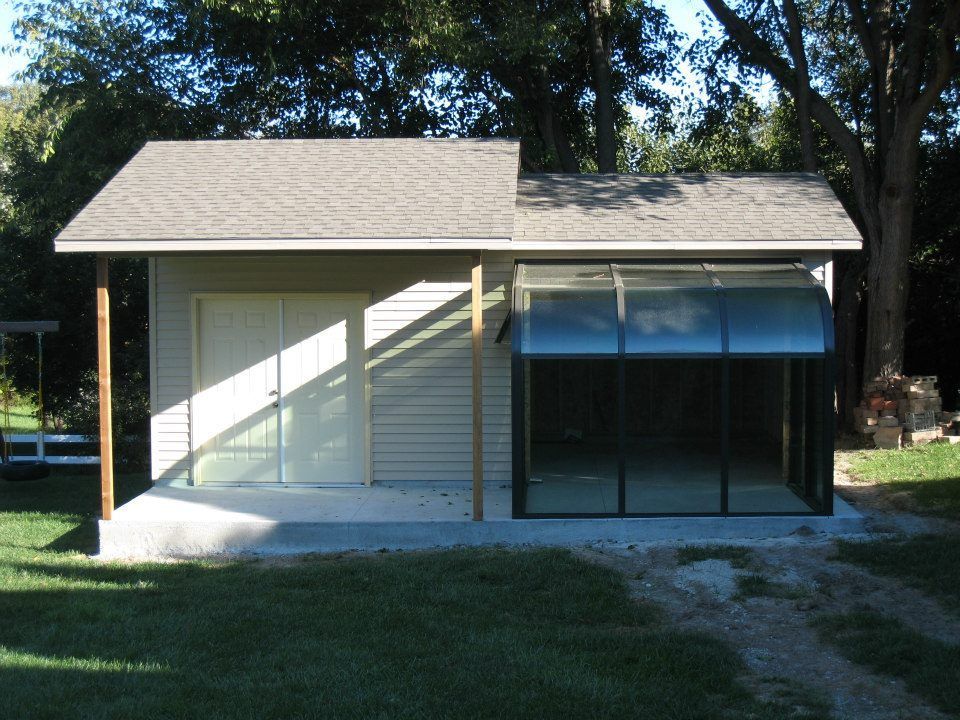 A small beige building with a glassed-in sunroom addition, set in a grassy yard.