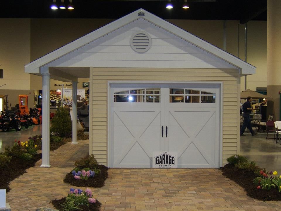 Tan and white garage with a small porch, set on a brick pathway, surrounded by flowers.