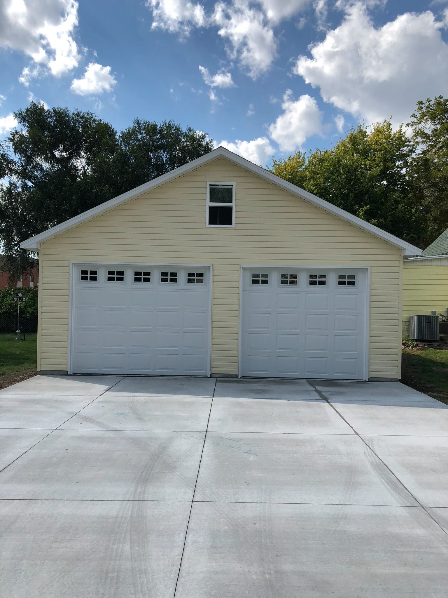 Two-car garage with two white doors, light yellow siding, and a concrete driveway under a cloudy sky.