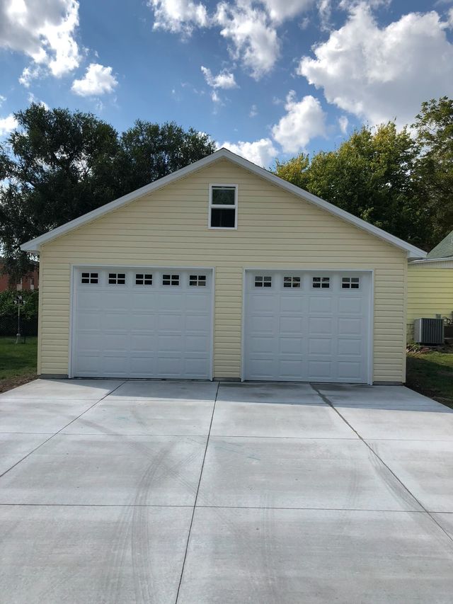 Two-car garage with white doors and light yellow siding, set on a concrete driveway, under a partly cloudy sky.