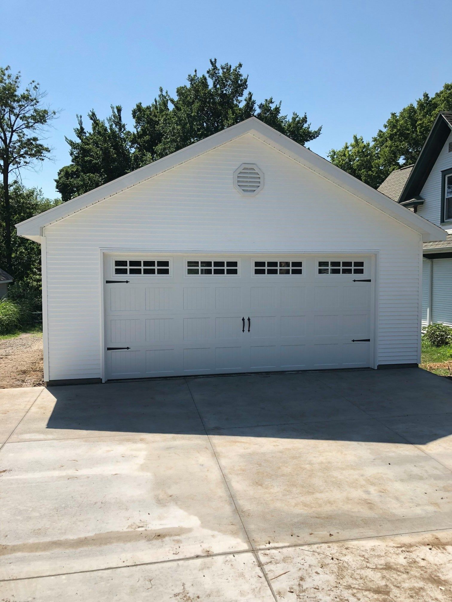 White garage with a concrete driveway against a blue sky, trees in the background.