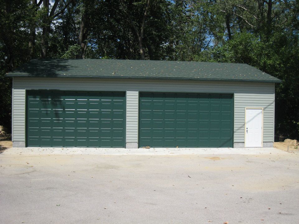 Two-car garage with green doors and a white side door, set against a backdrop of trees.