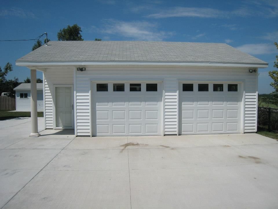 White two-car garage with a side door and attached carport under a blue sky. Concrete driveway.