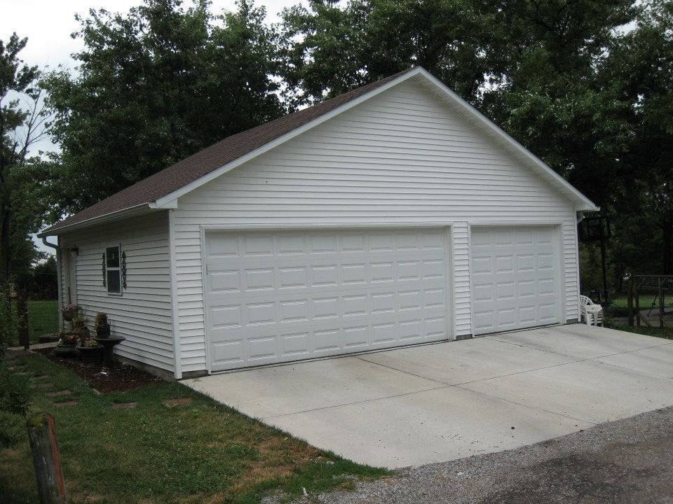 Two-car white garage with concrete driveway; set in a yard, trees in the background.