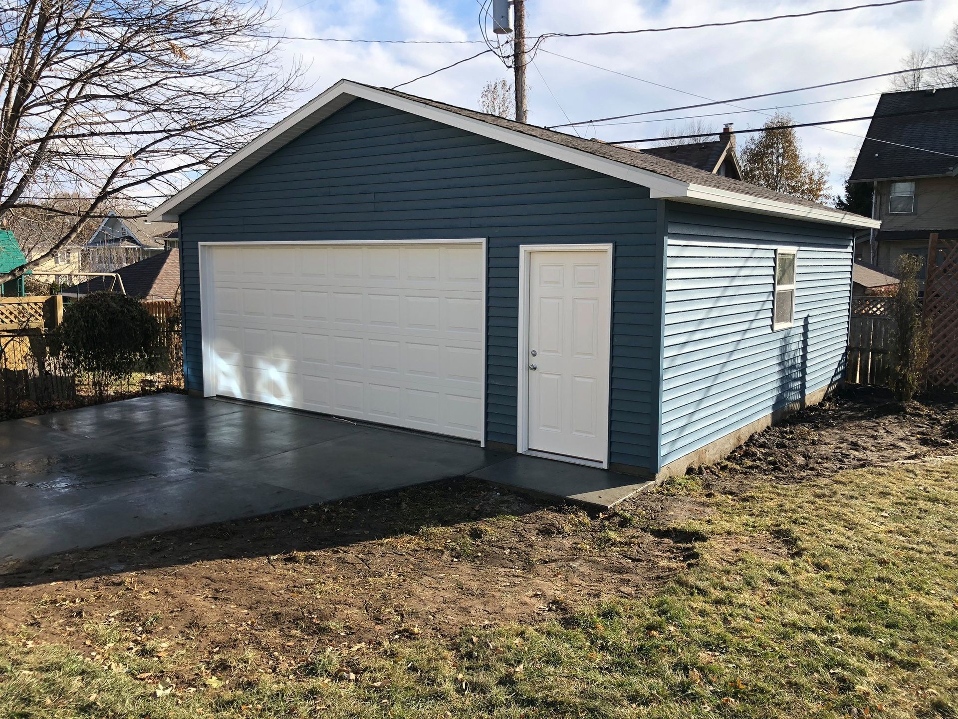 Blue-sided garage with white door and overhead door on a concrete pad with a lawn.