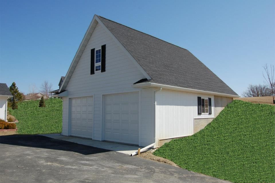 Two-car white garage with black shutters and dark gray roof, situated on a grassy hill.