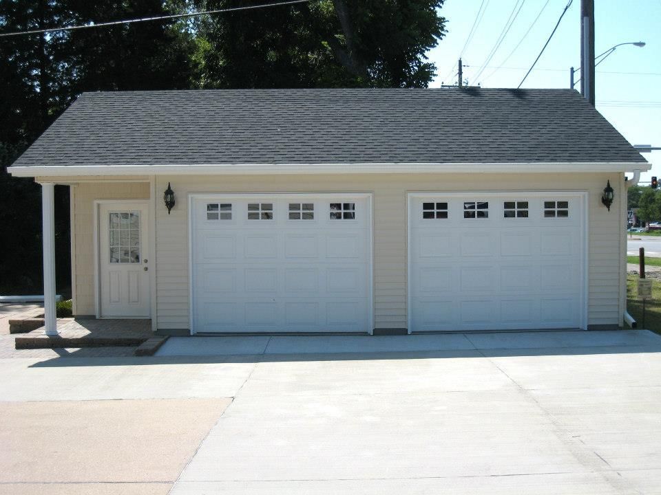 Two-car garage with white doors, light-colored siding, and a black roof on a concrete driveway.