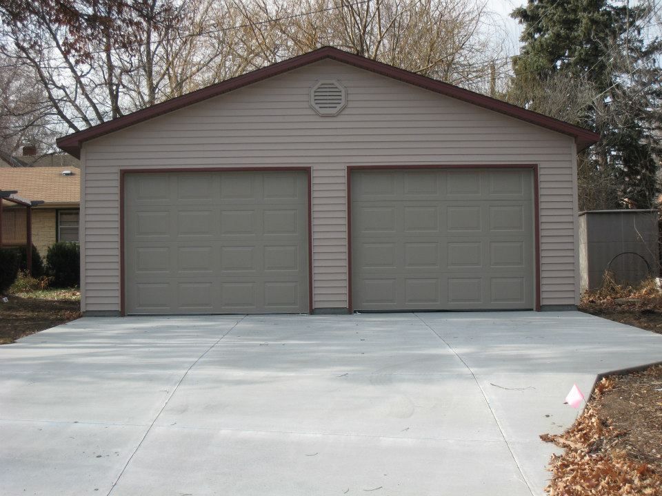 Two-car garage with tan siding, brown trim, and concrete driveway.
