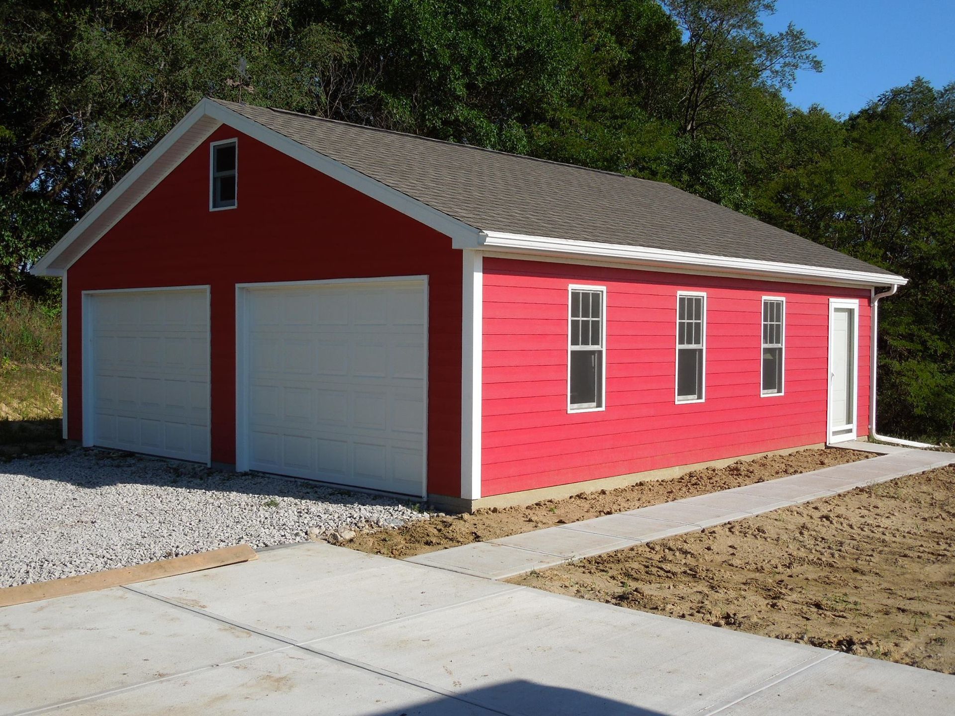 Red two-car garage with white doors, windows, and trim; gravel driveway and concrete path.