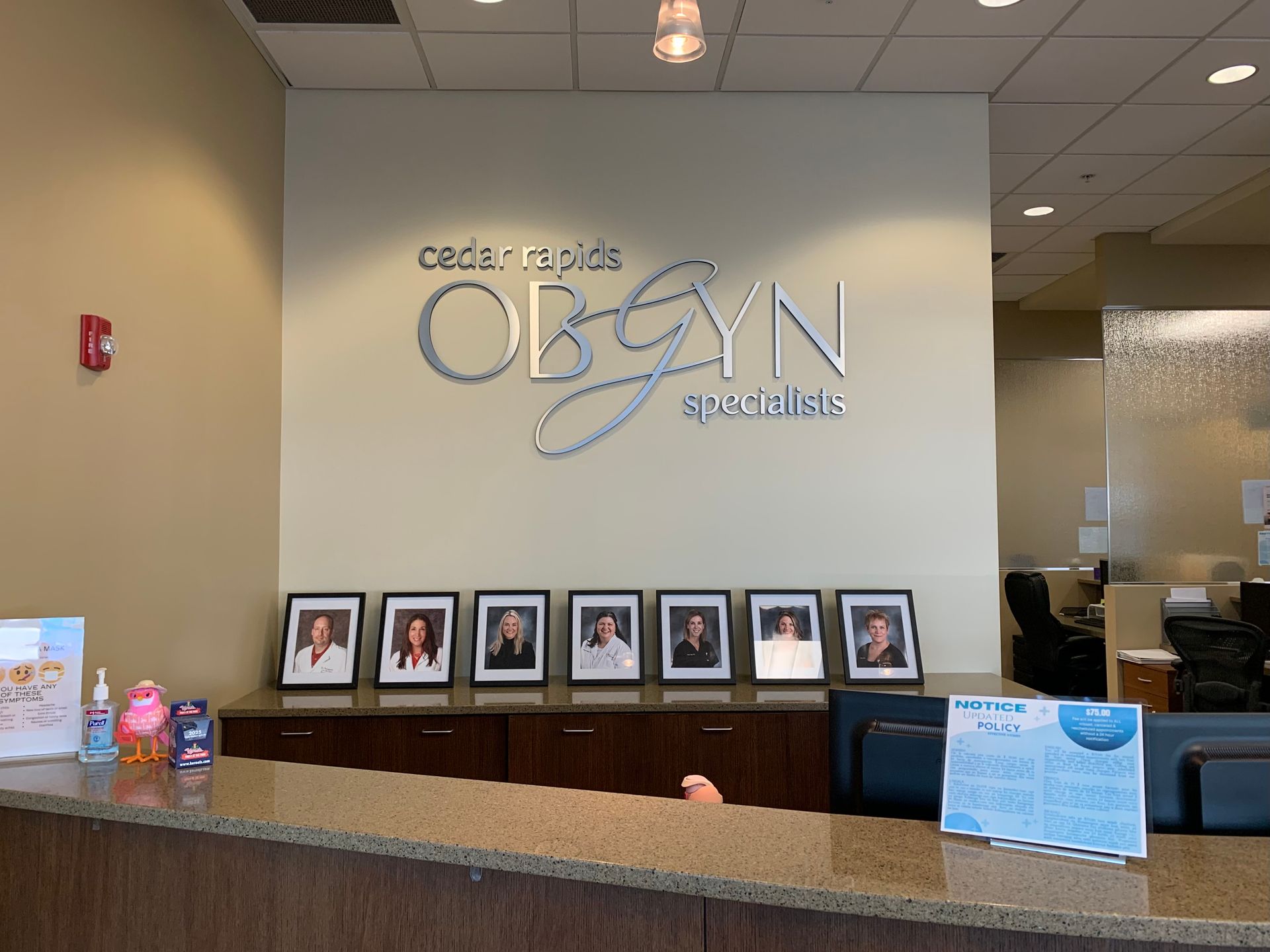 Reception desk in OB/GYN office with sign, staff photos, and information displays.