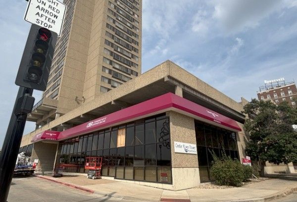 A commercial building with a red awning, next to a tall apartment building, under a cloudy sky.