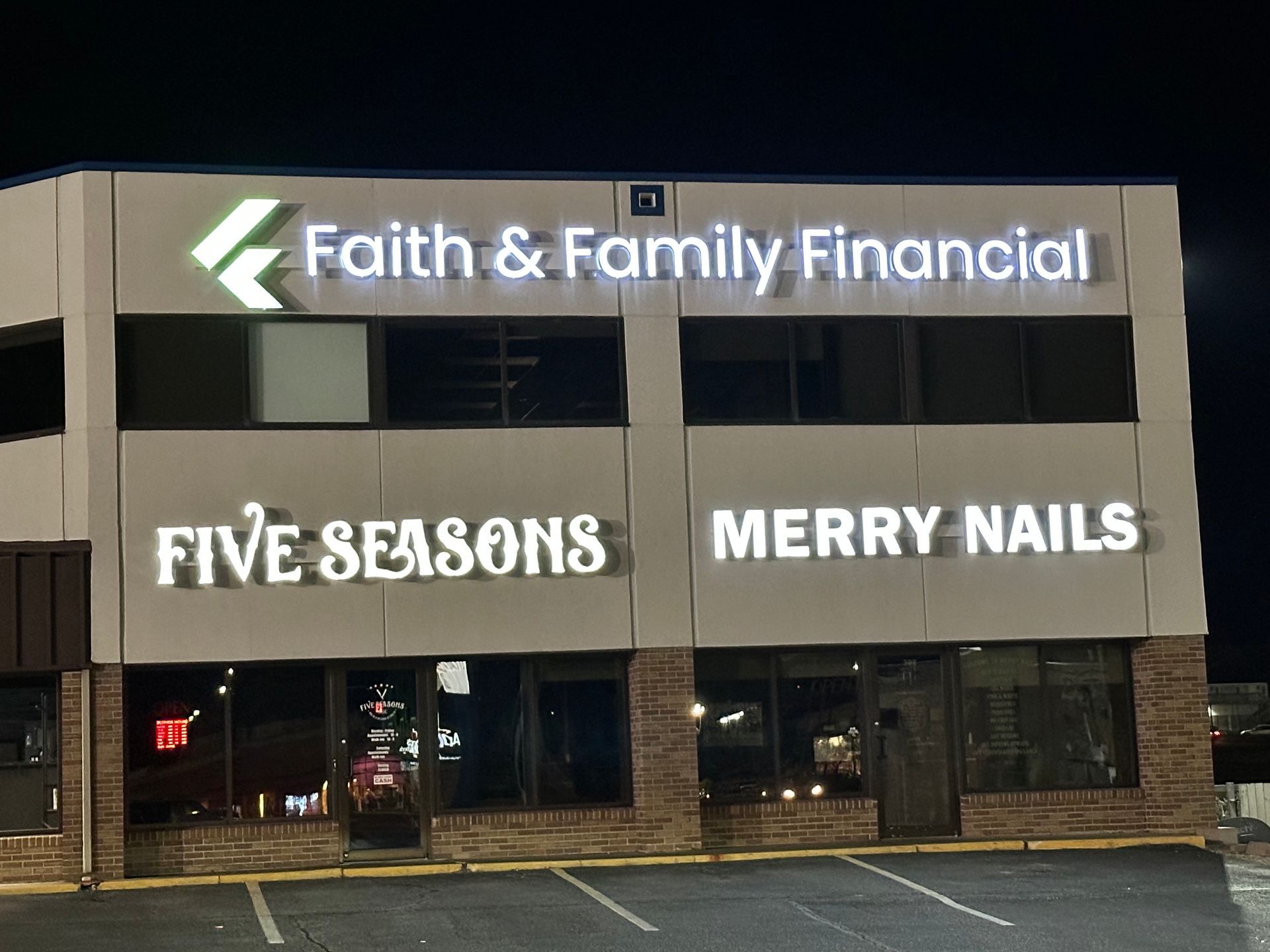 Building with signs: Faith & Family Financial, Five Seasons, Merry Nails. Night setting, illuminated signs.