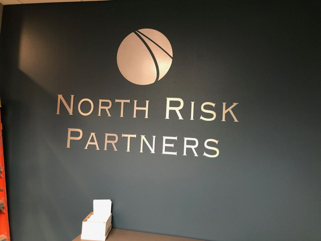 Logo for North Risk Partners on a teal wall; silver lettering and a globe graphic.