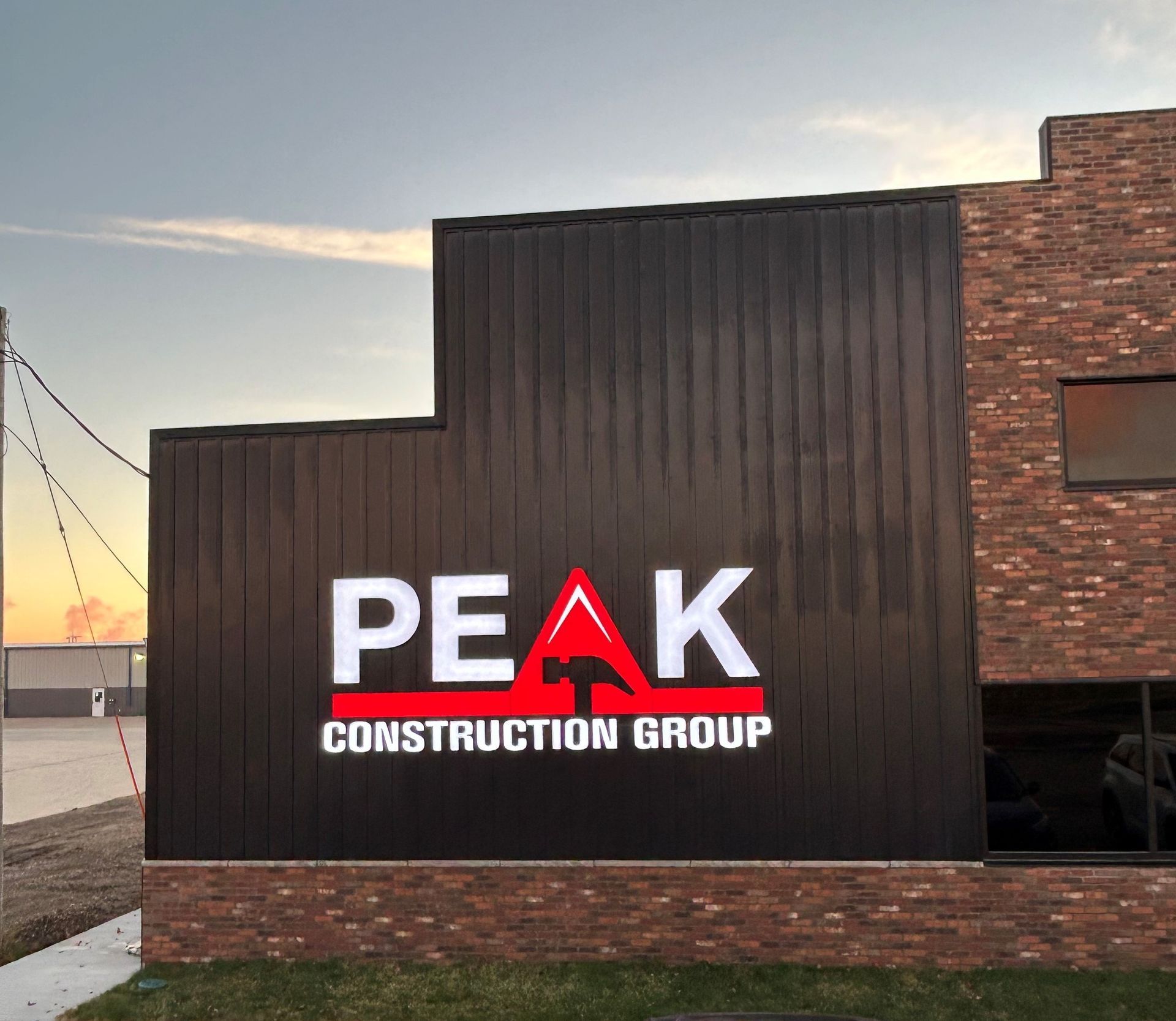 Sign for Peak Construction Group on a brick and black building, white letters, red hammer icon.
