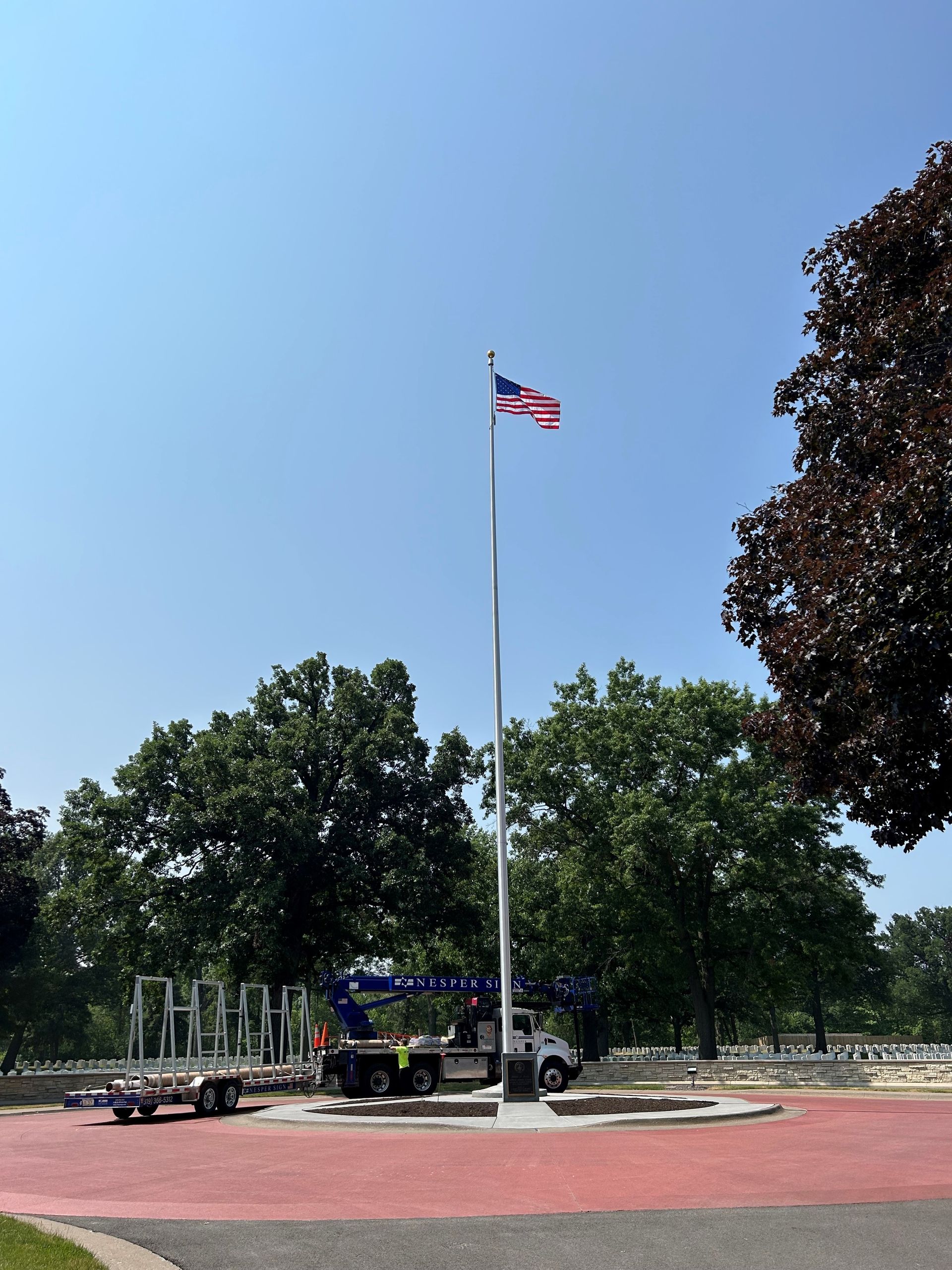 American flag flying on a tall pole, with trees and a crane in the background.