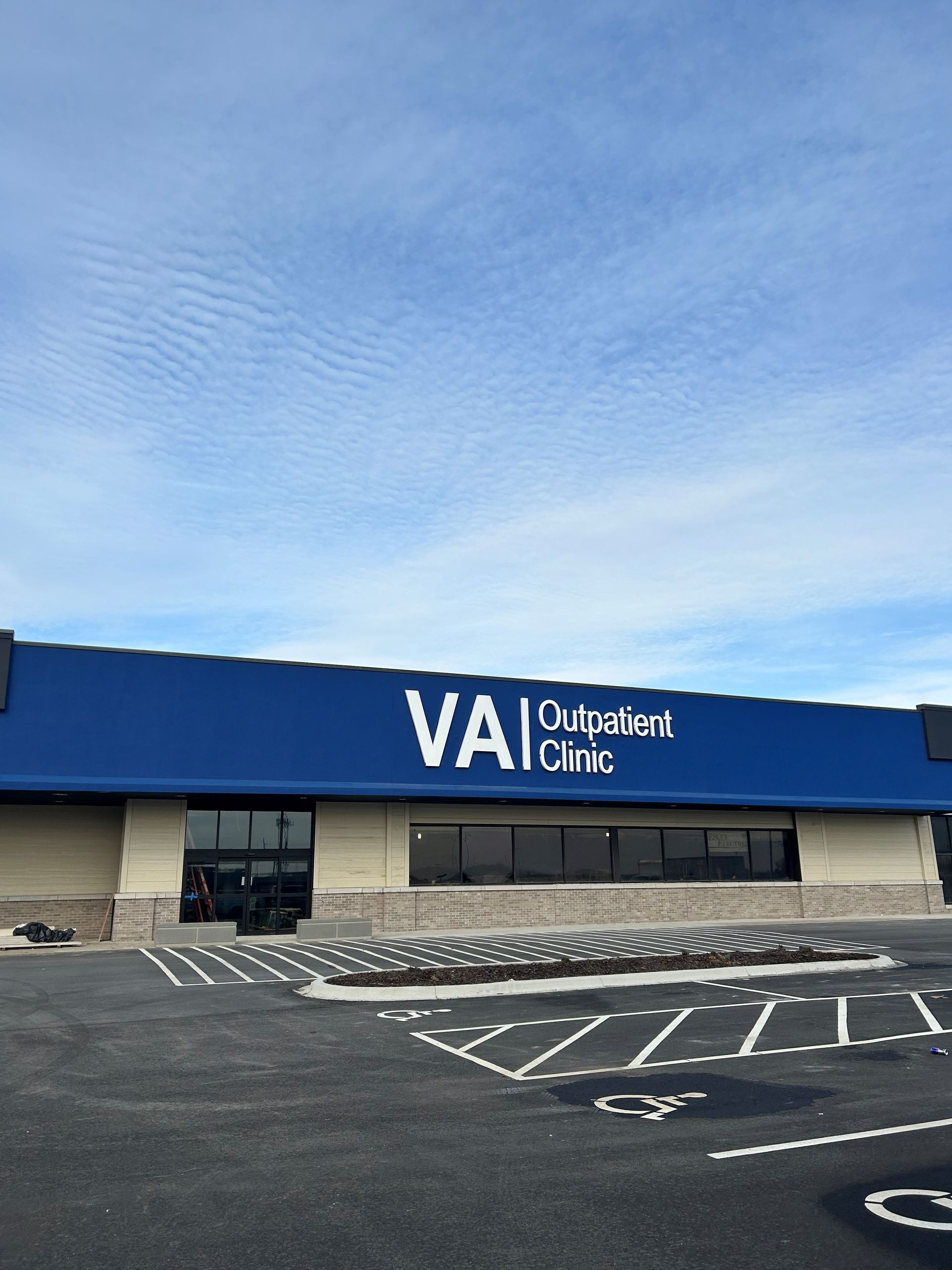 VA Outpatient Clinic with blue roof and lettering, beige building, and parking spaces.