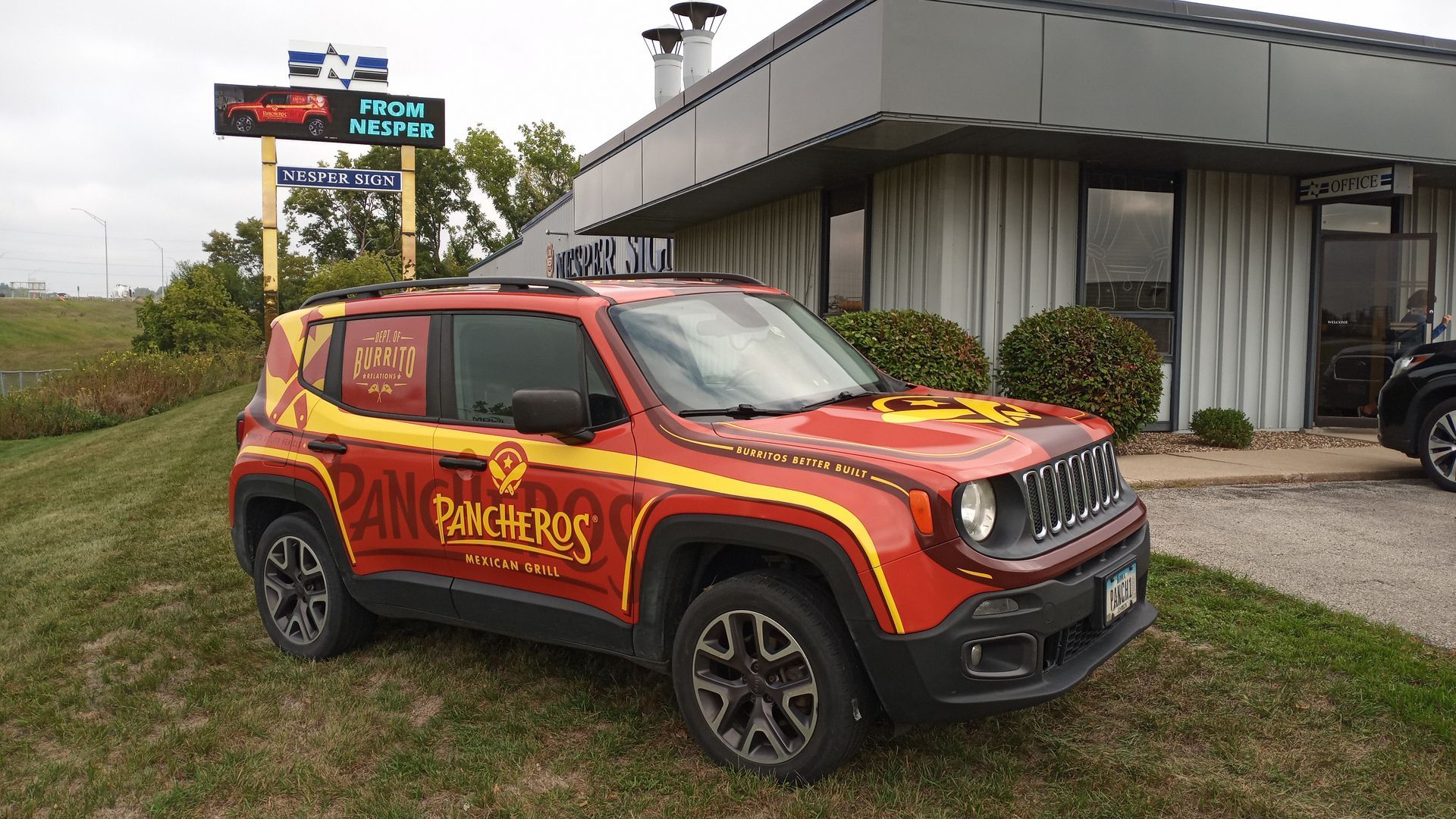 A red jeep renegade is parked in front of a building.