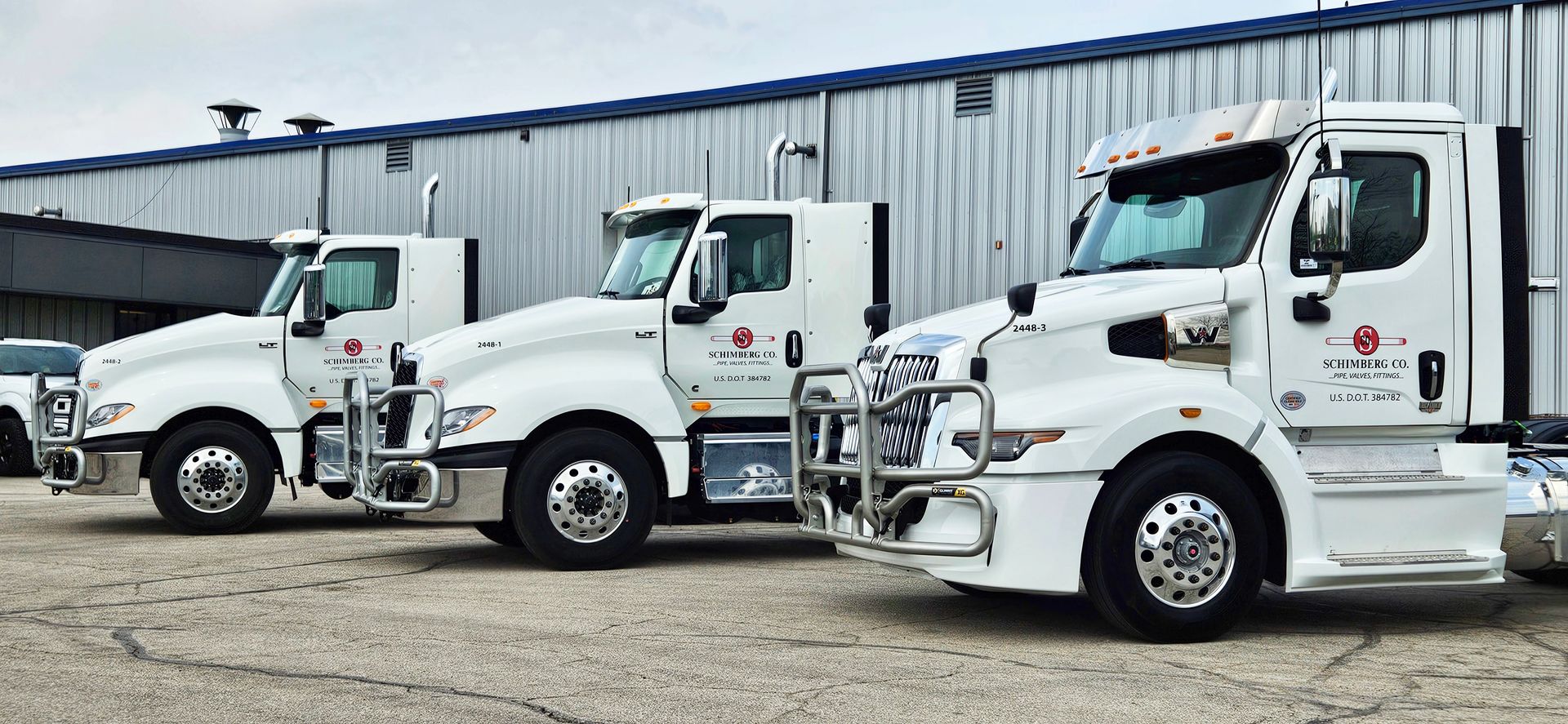 Three white semi trucks are parked in front of a building.