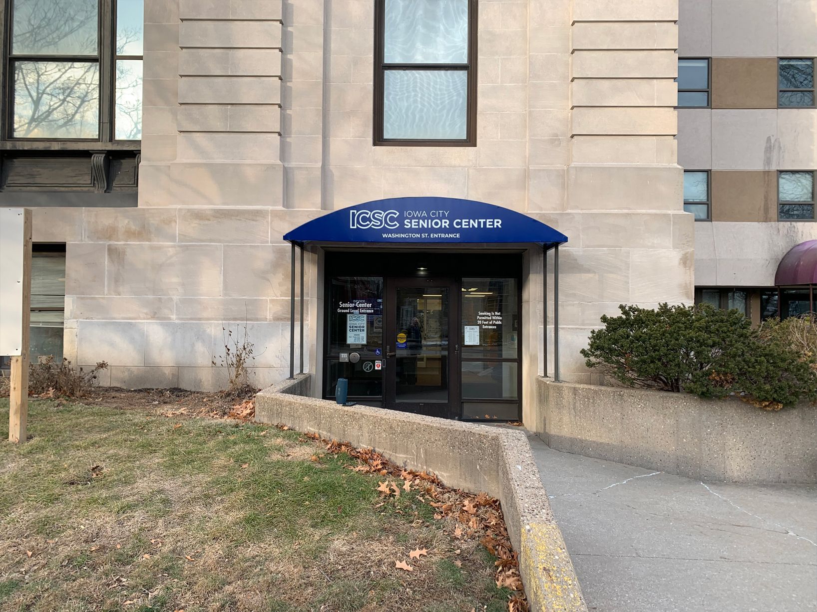 Entrance to the Autism Center with blue awning, glass doors, and a concrete ramp on a sunny day.