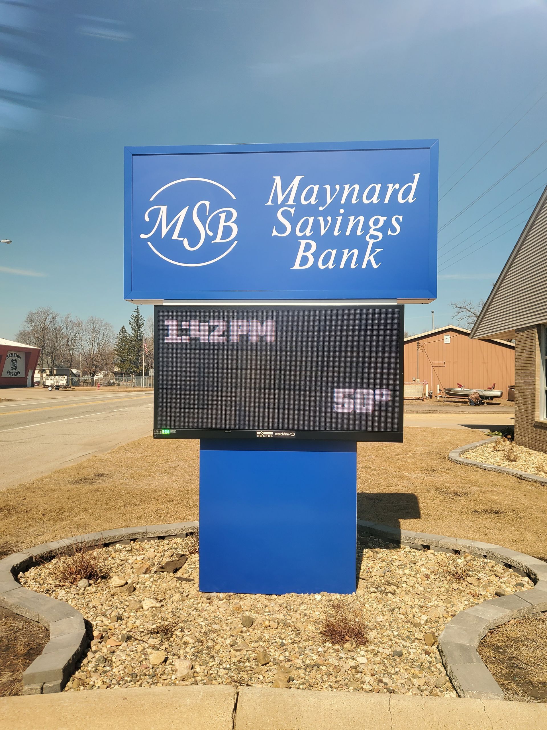 Blue sign for Maynard Savings Bank with LED display showing 1:42 PM and 50 degrees.