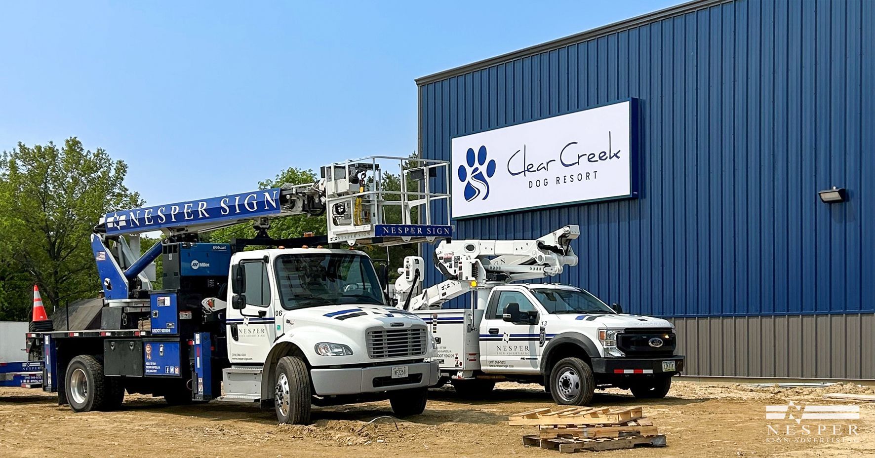 Two white trucks with lift arms next to a blue building with a sign.