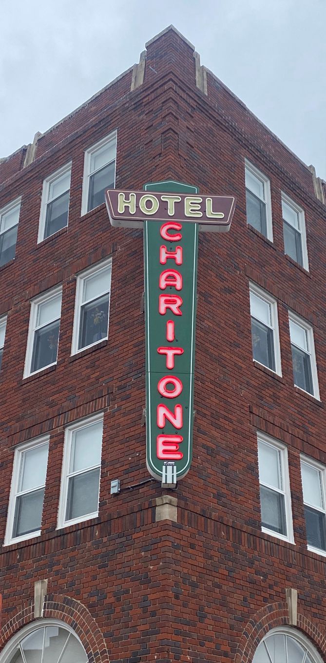 Corner view of the Hotel Charitone building with a large neon sign against a cloudy sky.
