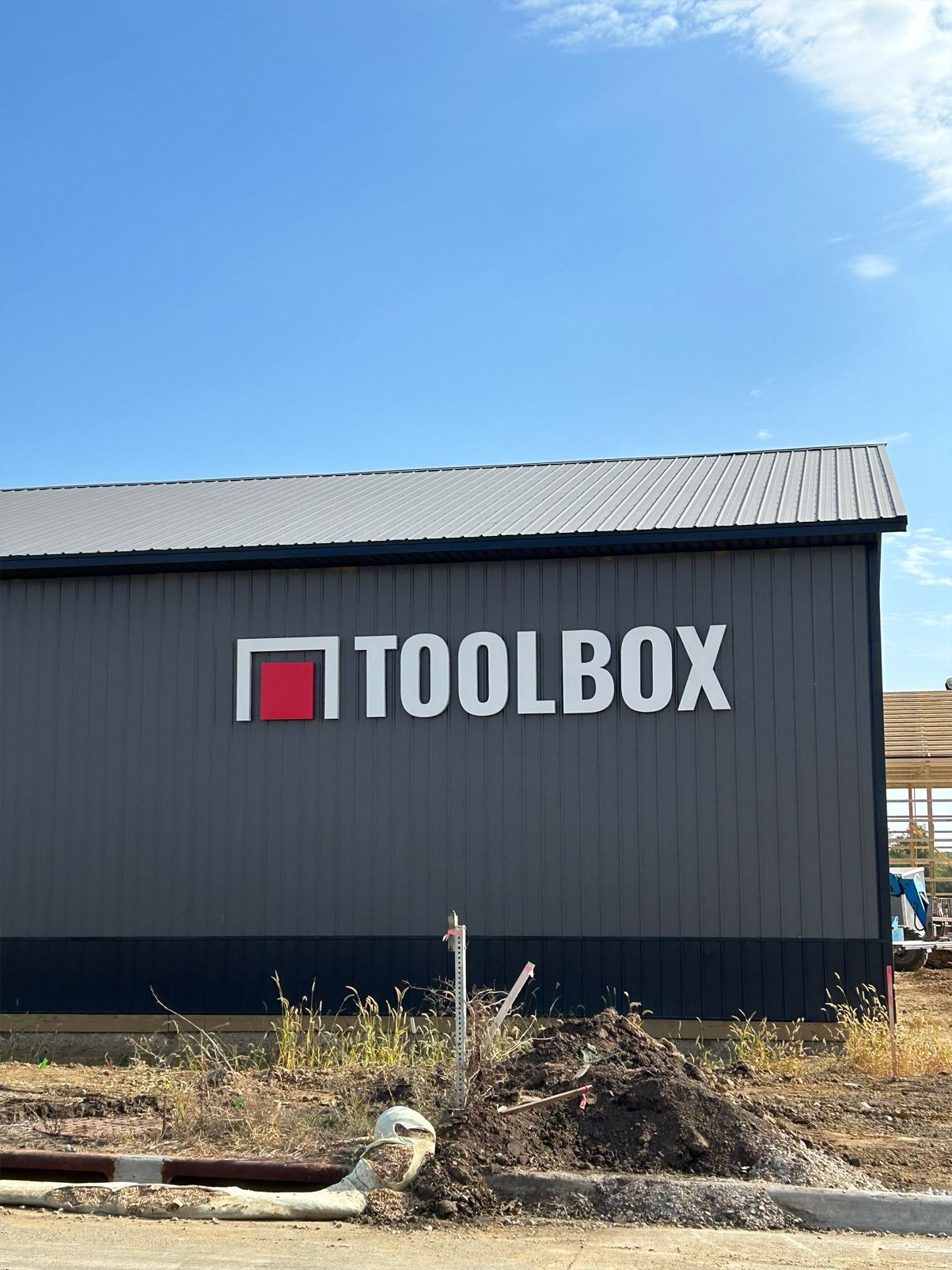 Gray building with a TOOLBOX sign; white letters, red and white square. Sunny day, blue sky.