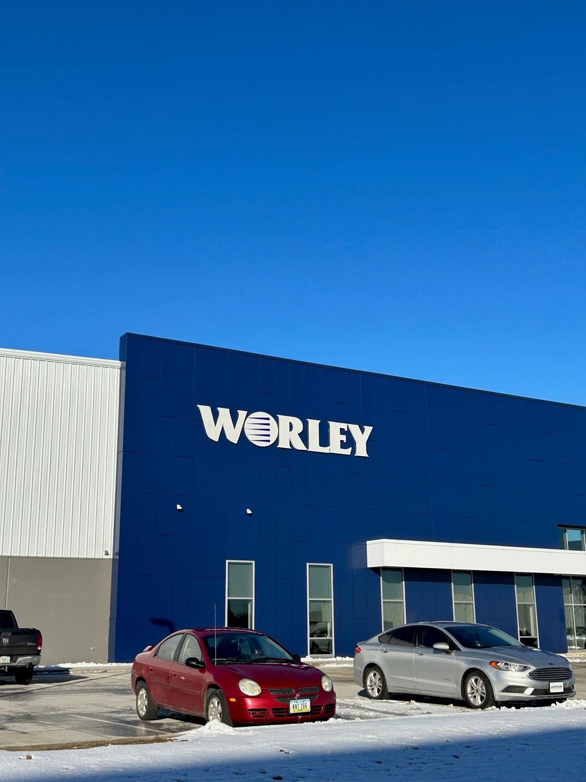 Worley building, blue exterior, cars parked in front, snow on the ground, blue sky.