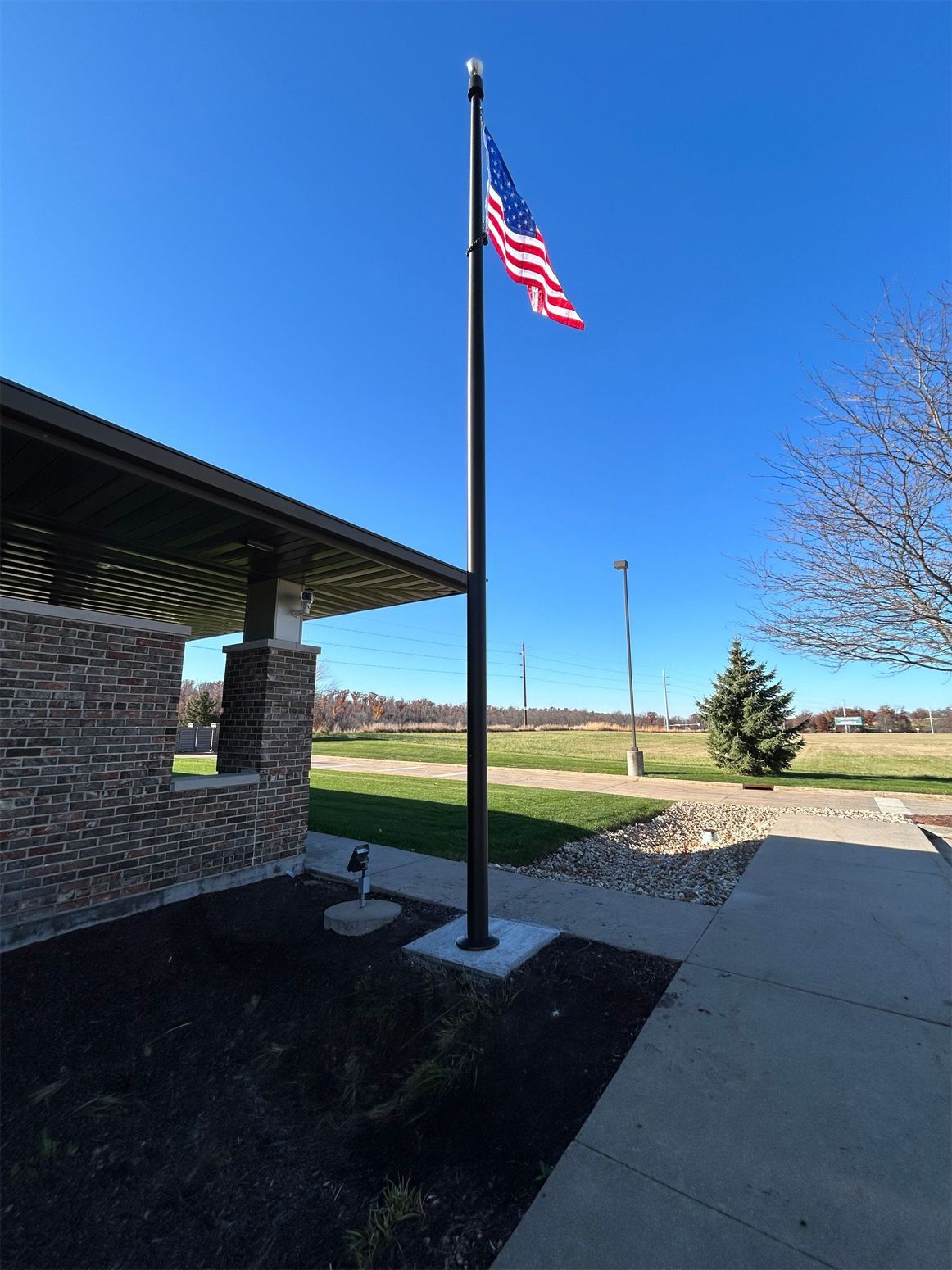 American flag flying on a tall pole in front of a building on a sunny day.