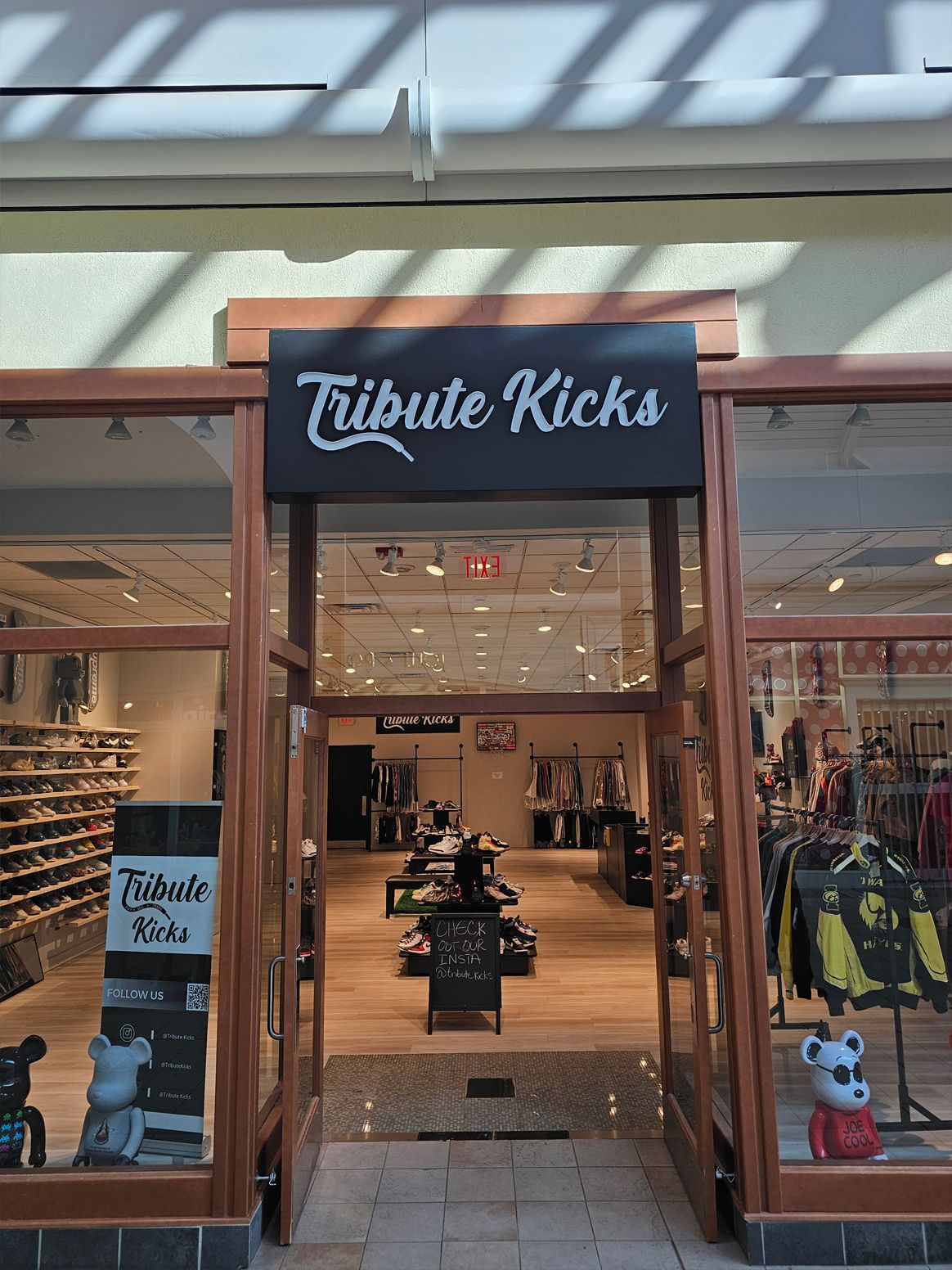 Tribute Kicks store front with sign. Interior view of sneakers, clothing. Shopping mall setting.