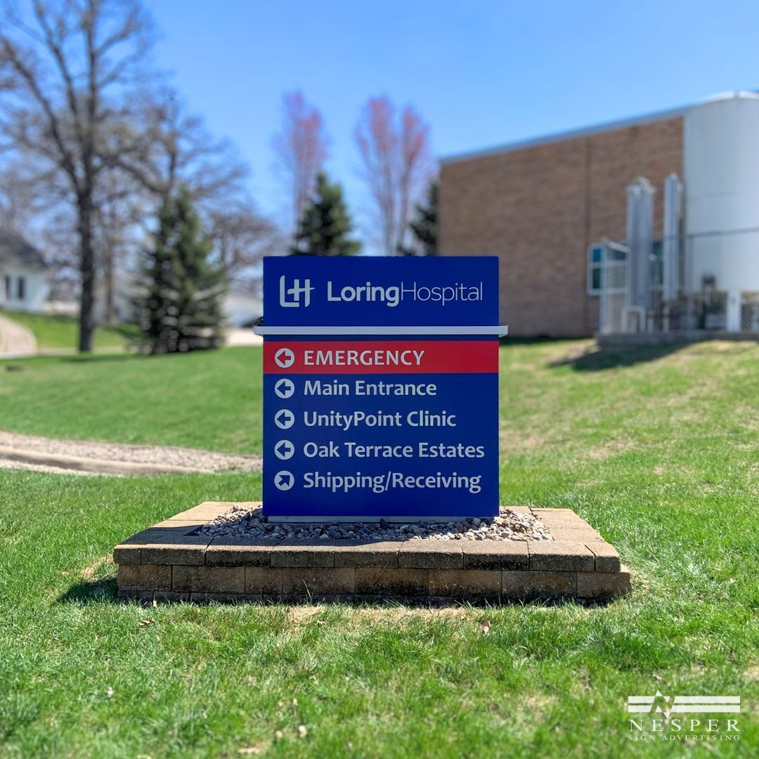 A monument sign for Loring Hospital is sitting in the grass in front of a brick building.