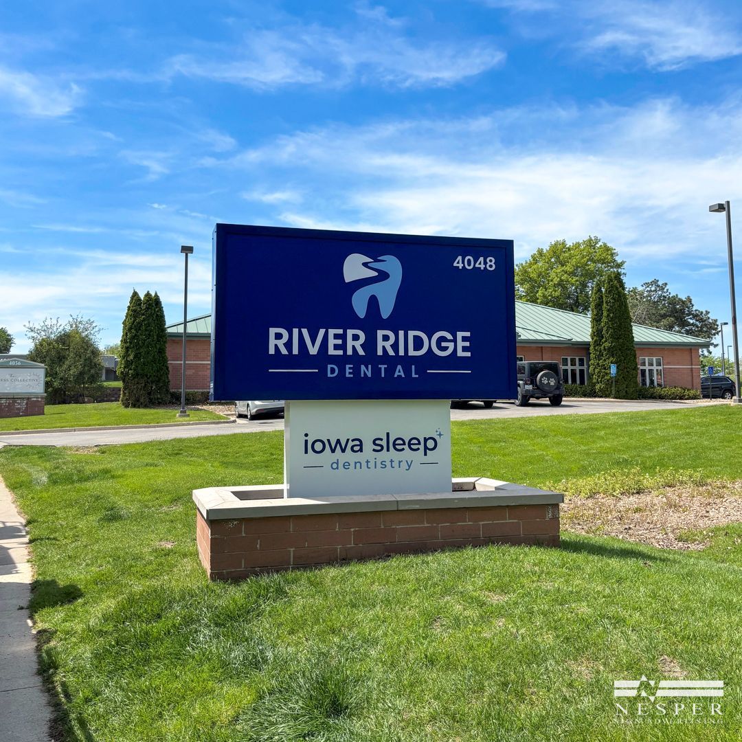 Sign for River Ridge Dental and Iowa Sleep Center. Blue and white sign with building in background.