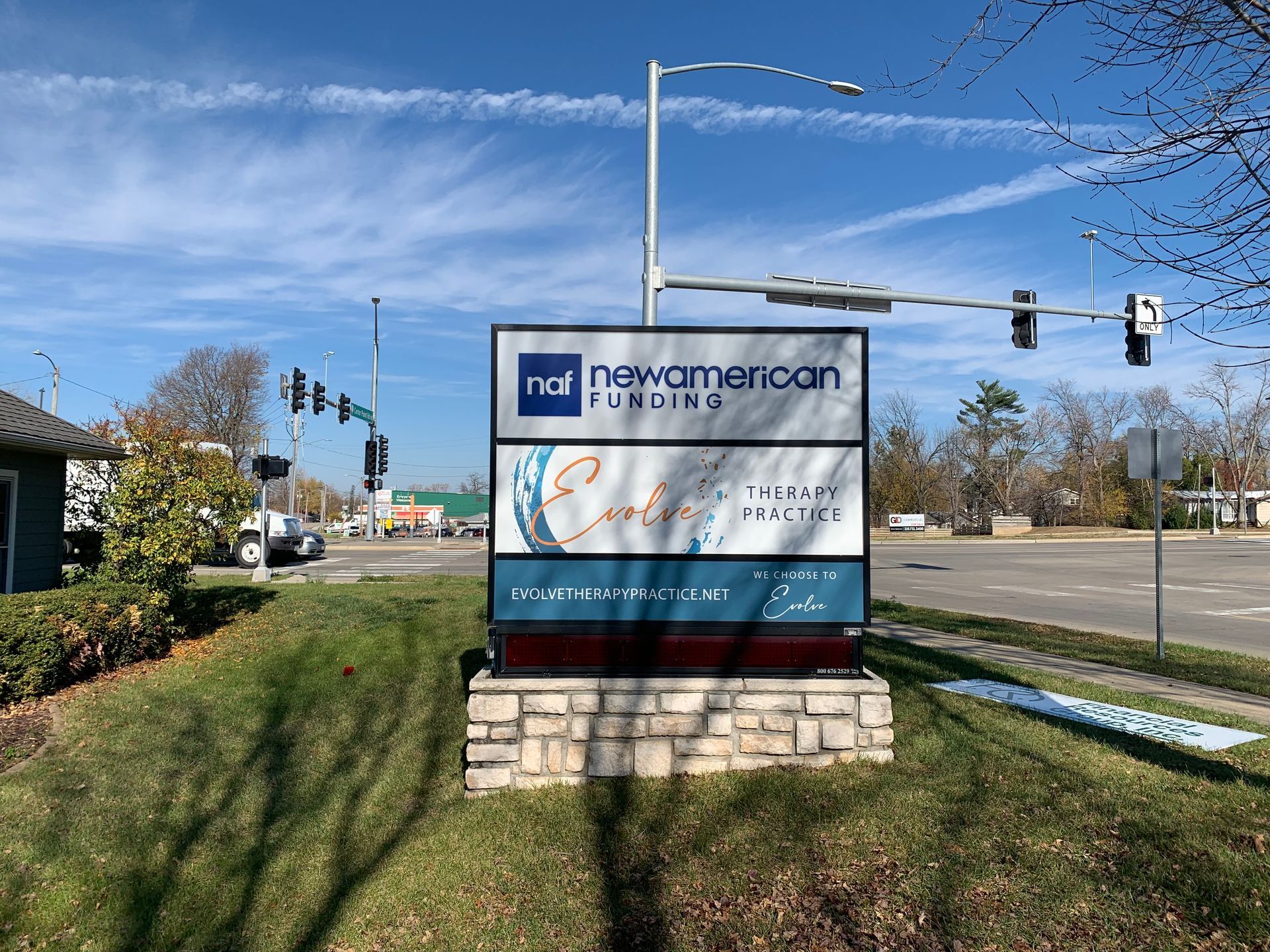 Sign with New American Funding and other businesses on a street corner under a blue sky.