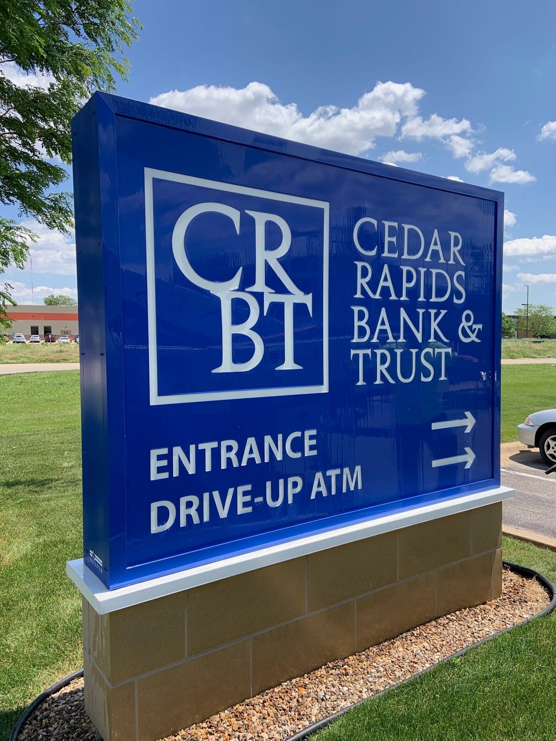 Blue CRBT bank sign with white text, entrance & ATM directions, on a brick base, outdoors.