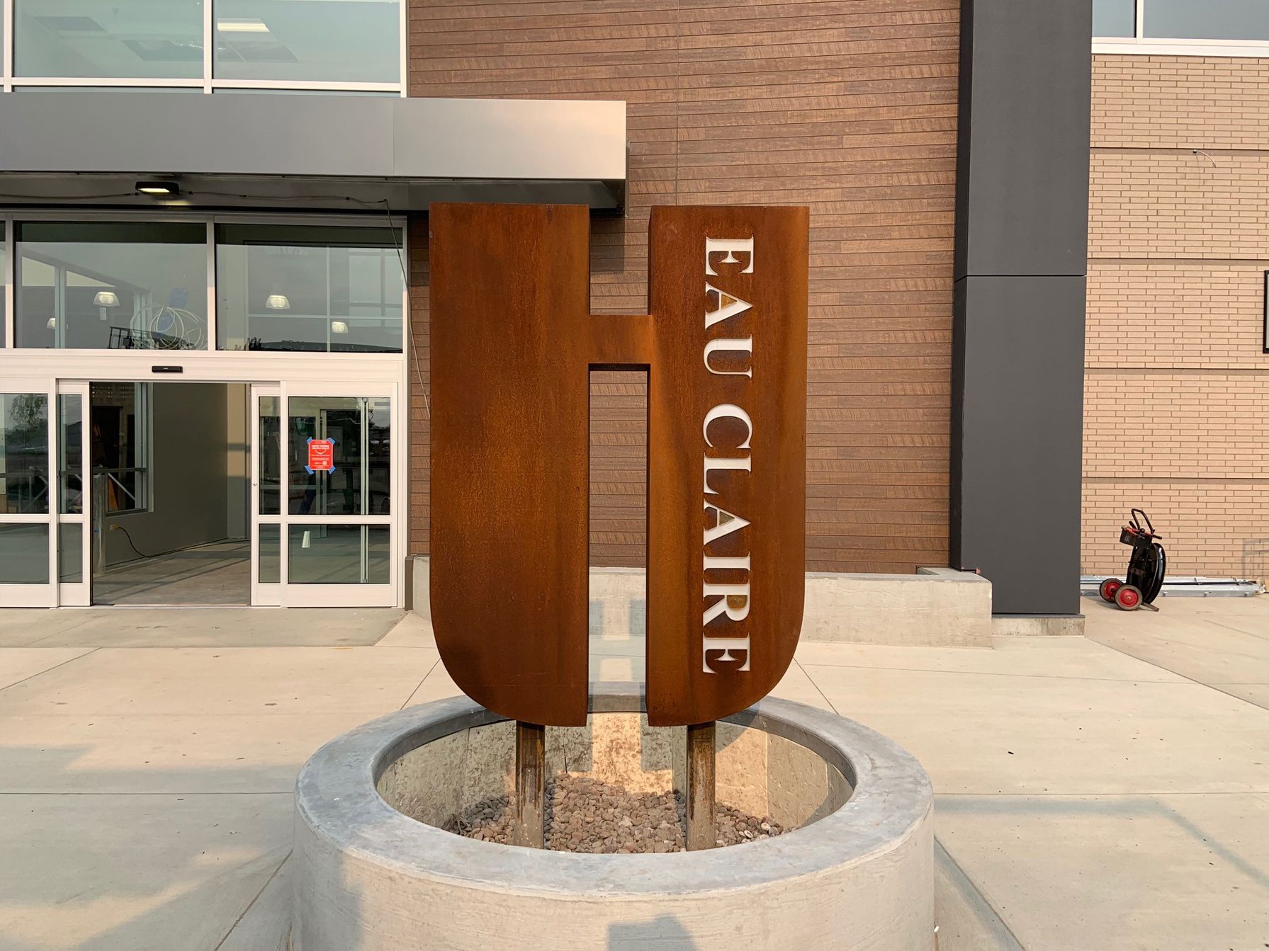Rust-colored 'Eau Claire' sign outside a modern building with glass doors; person in black jacket.