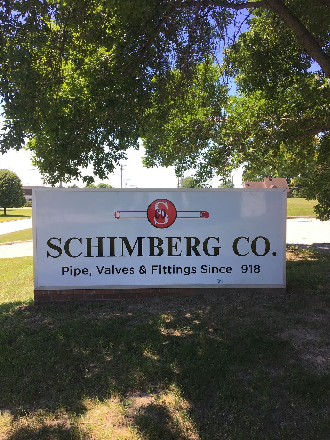 Sign for Schimberg Co., white with company name and logo, 'Pipe, Valves & Fittings Since 1918' on green lawn.