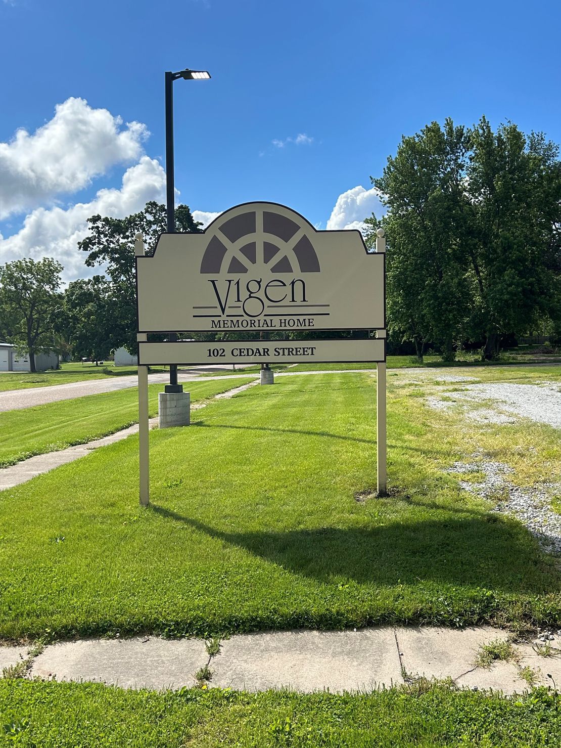 Sign for Vigen Center with logo on grass, near road and trees, sunny day.