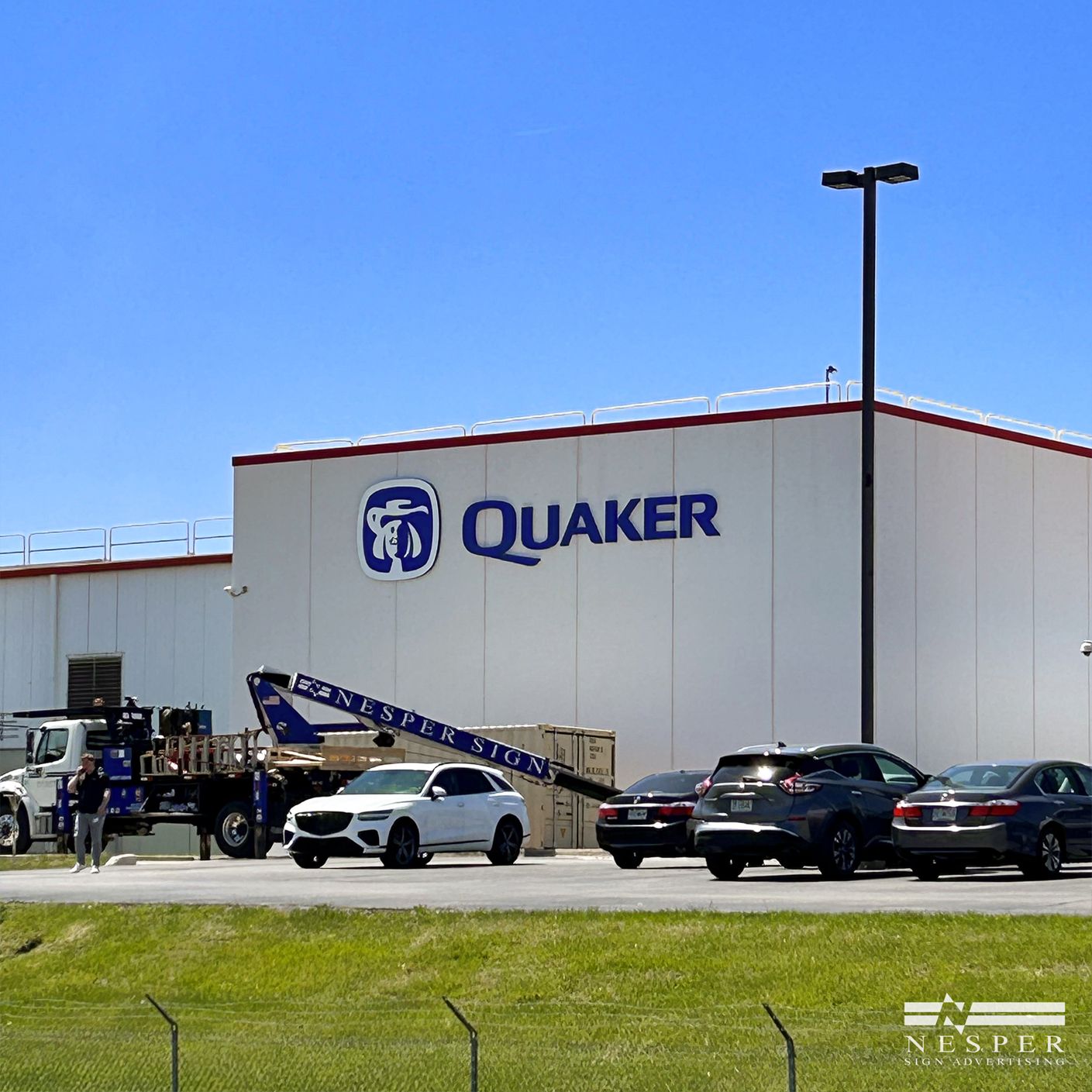 Quaker factory building with cars parked out front on a sunny day.