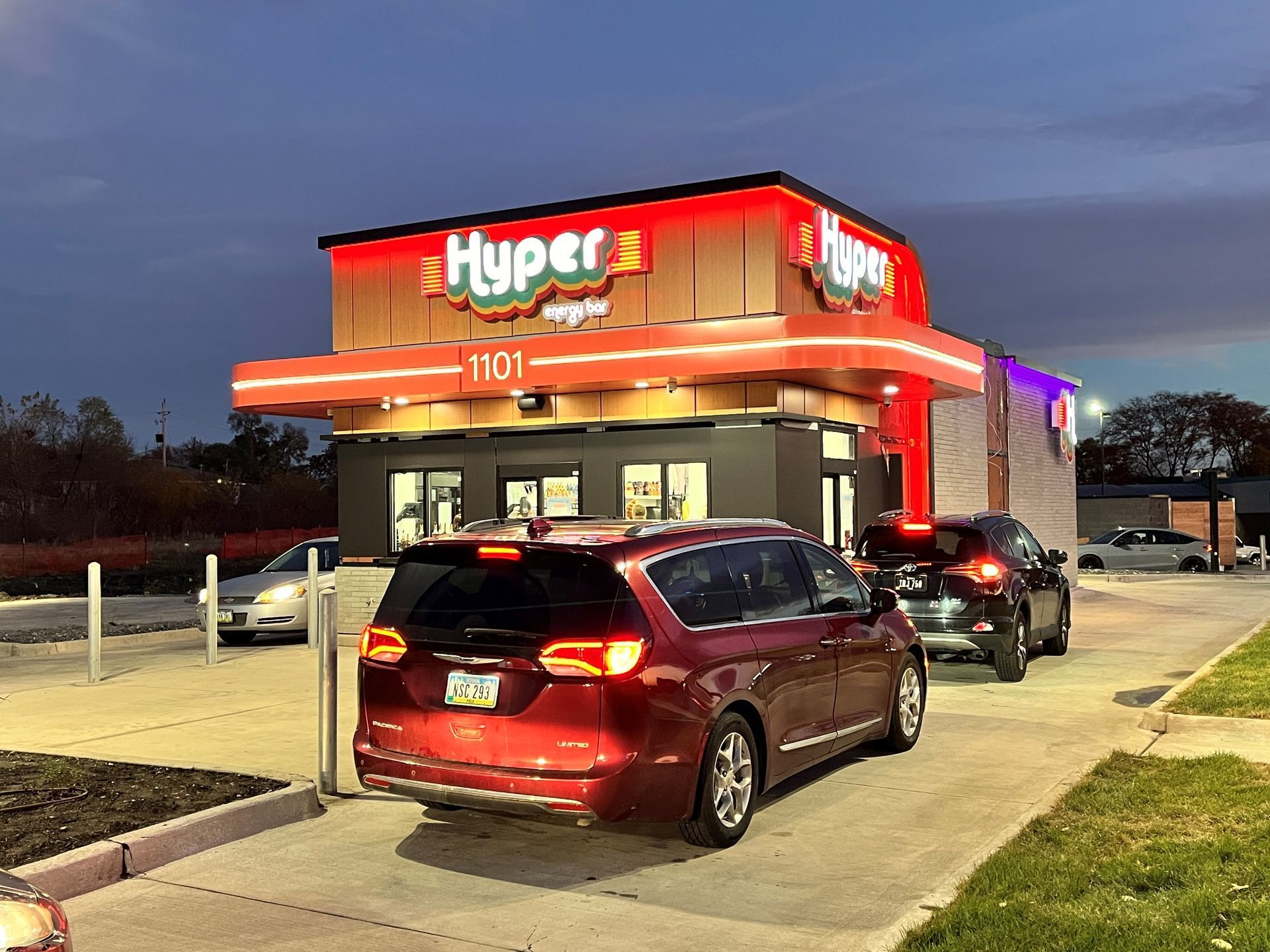 A drive-thru restaurant, Hyper, with cars in line; red and white signage, exterior at dusk.