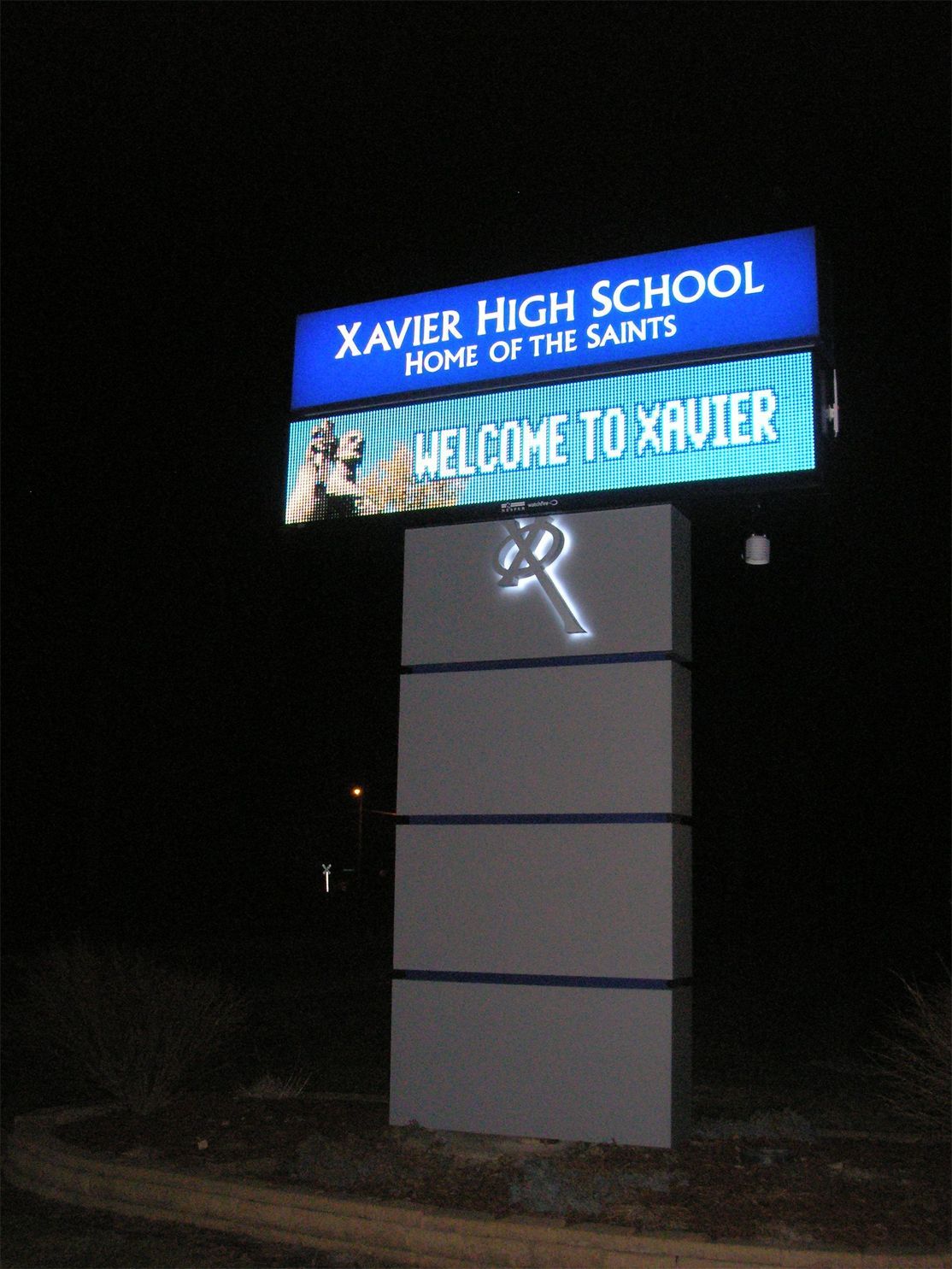 A sign for xavier high school is lit up at night