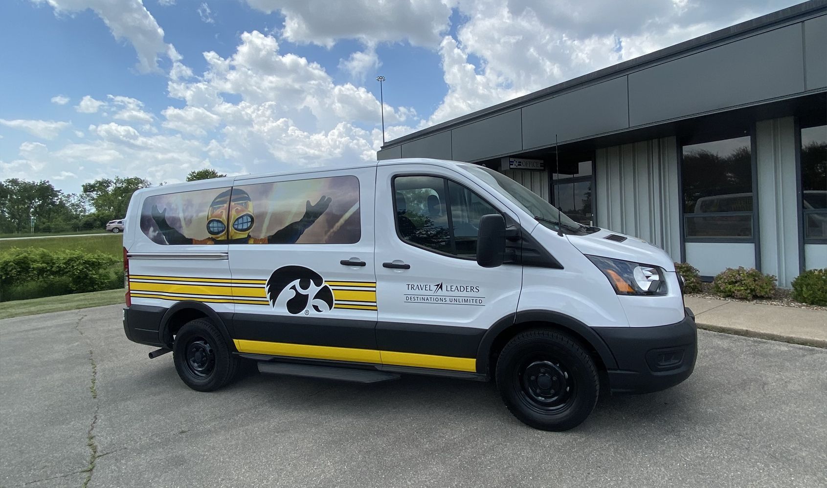 White van with black wheels and a yellow/black design parked outside a building.