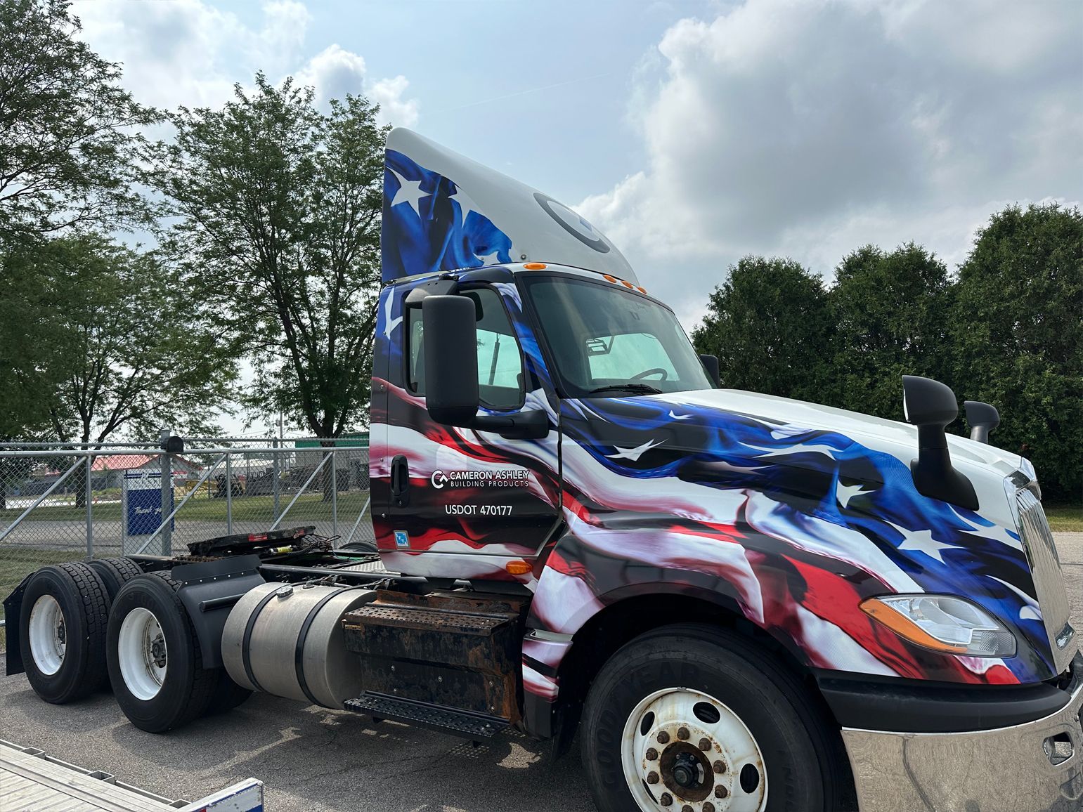Semi-truck with patriotic American flag design on the cab, parked outside on a cloudy day.