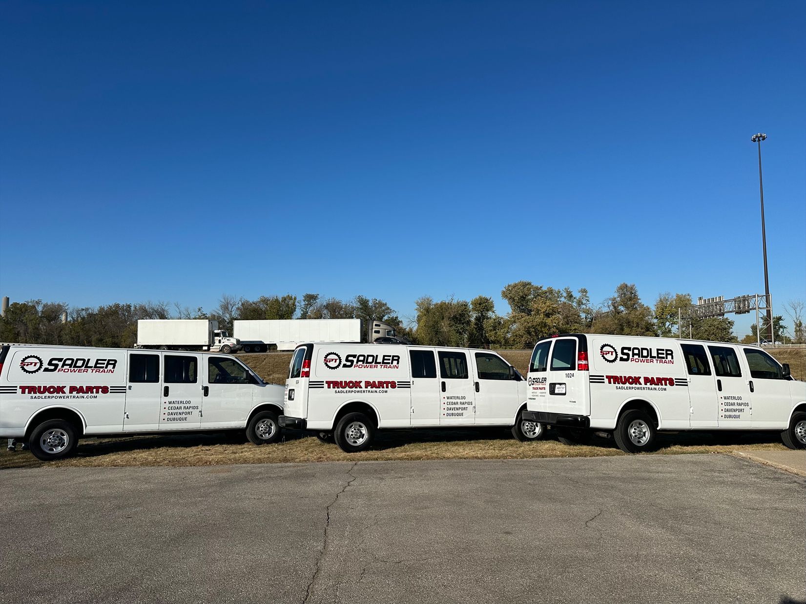 Three white vans with company logos parked outside on a sunny day.