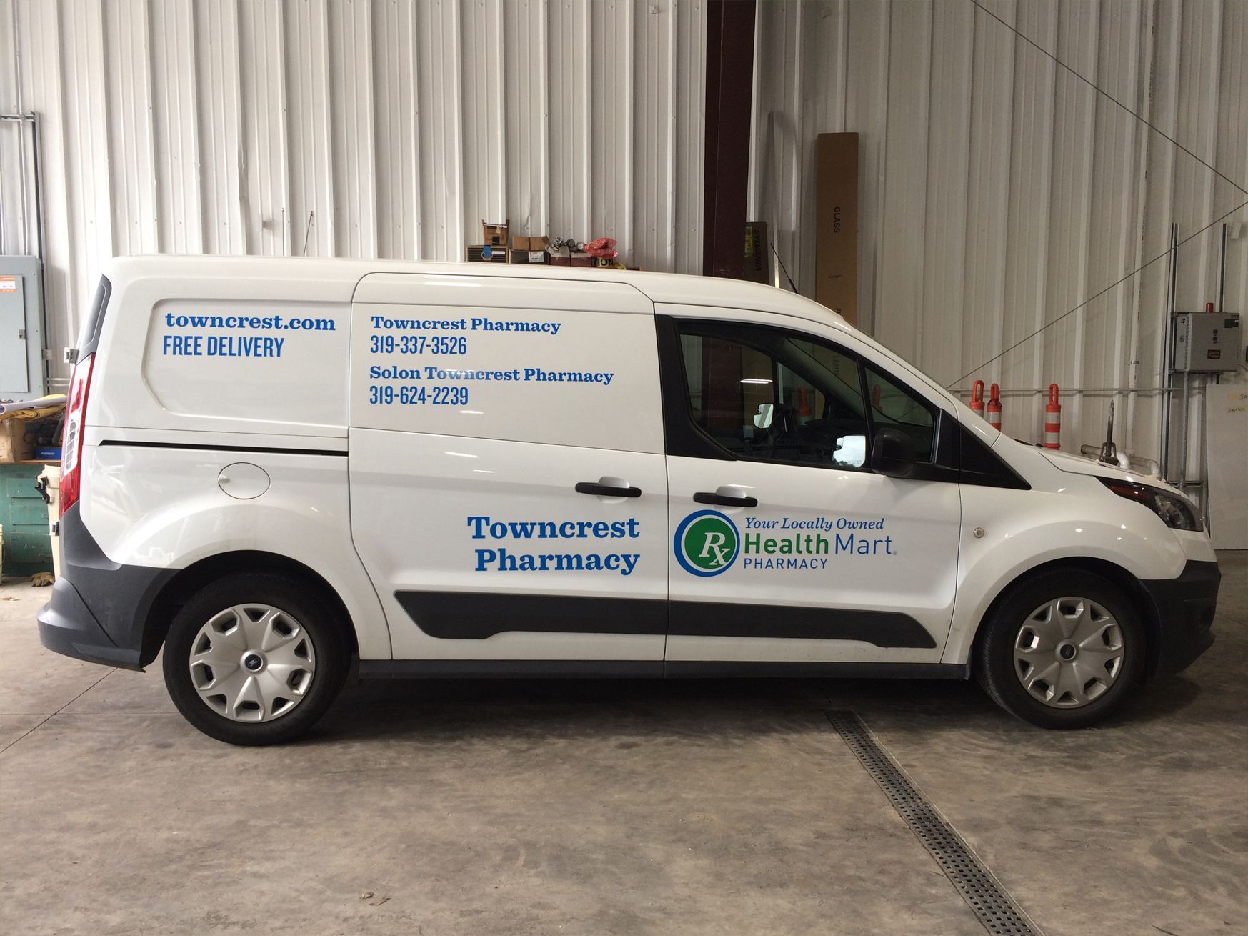 White delivery van for Towncrest Pharmacy with logo and contact info parked inside a building.