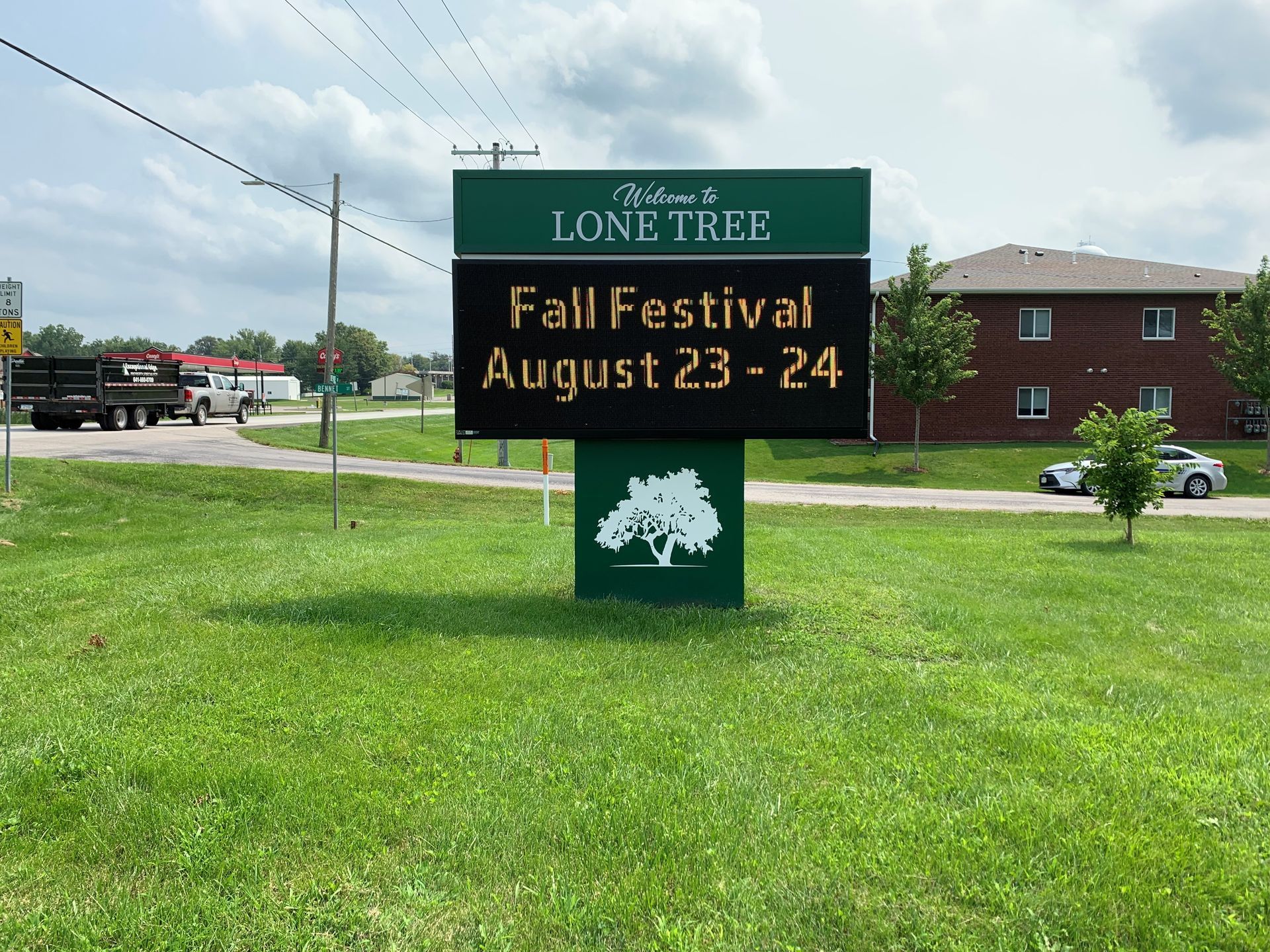 Sign for Lone Tree Fall Festival, August 23-24. Green sign with white text and a tree graphic.