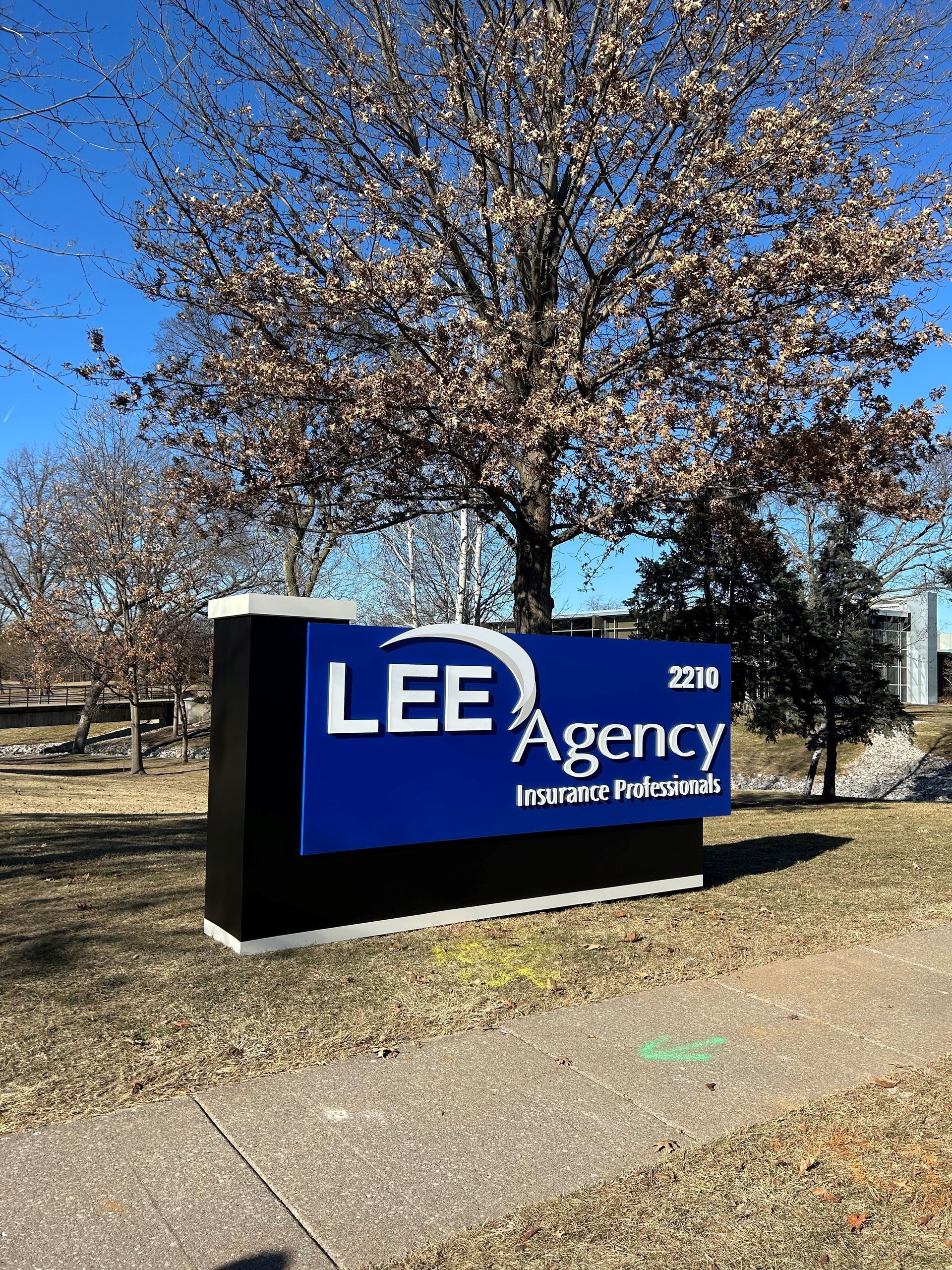 A blue and black sign for lee agency is in front of a tree.