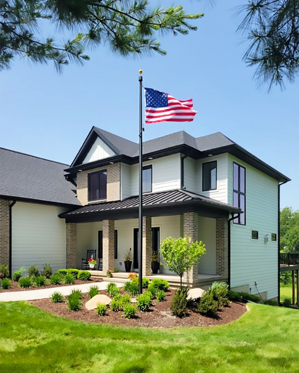Two-story house with an American flag waving on a flagpole in front. Green grass and blue sky.